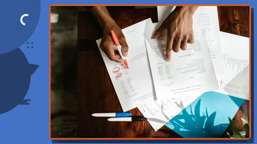 Hands marking up financial documents and statements on a desk.