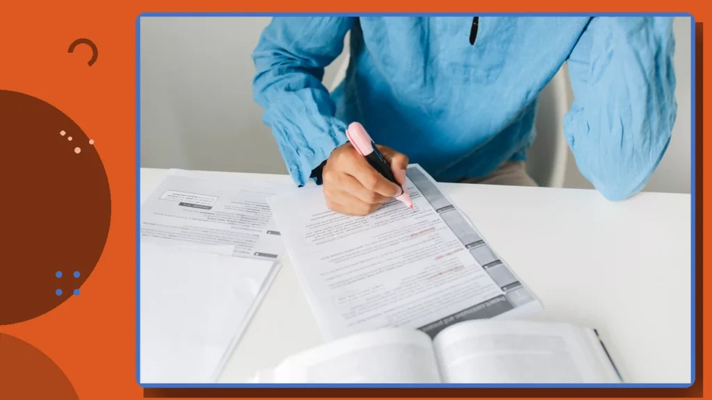 A person filling out legal forms at a desk with a book open beside them.